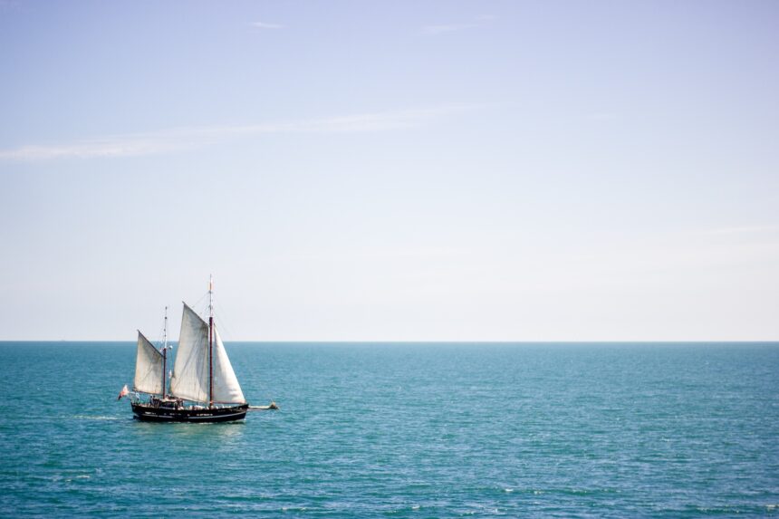 A sailing boat with white sails on a calm sea surface at daytime. Photo: Envato Elements